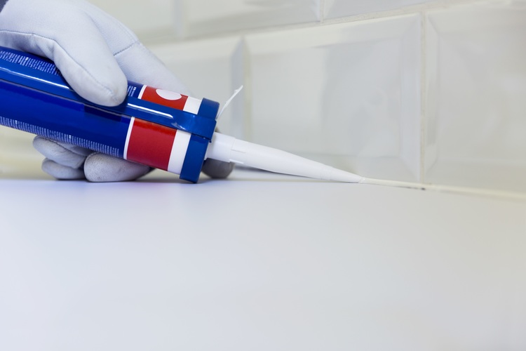 Plumber applying silicone sealant to the countertop and ceramic tile. Home improvement, kitchen renovation concept